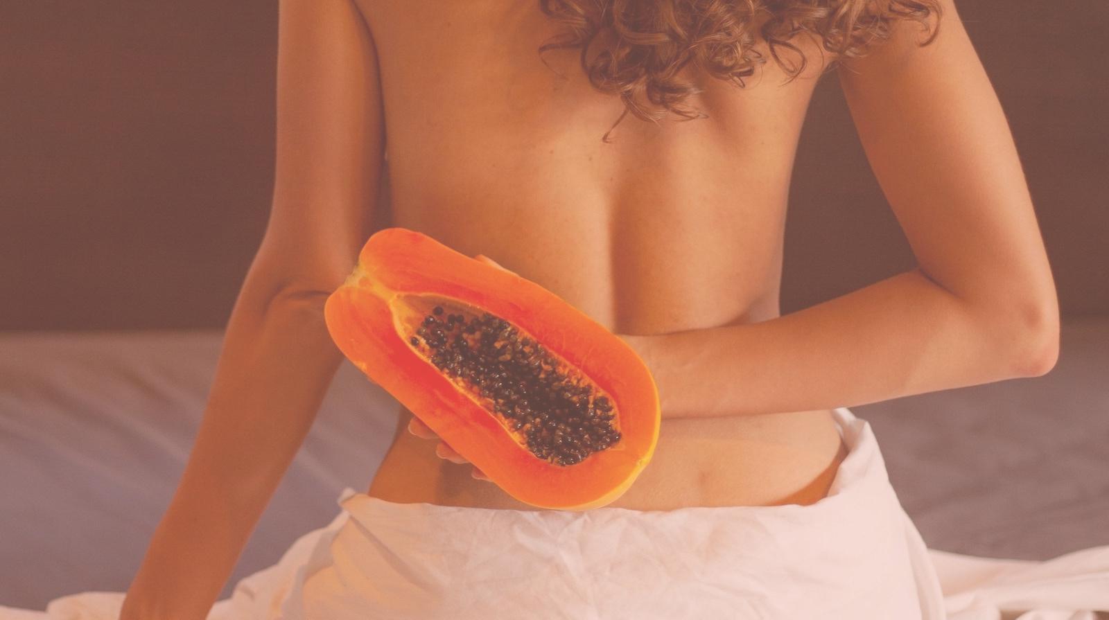 naked woman holds a papaya behind her back represent vulva