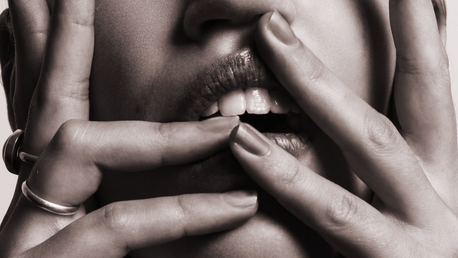 black and white photo of a woman's open mouth with her hands and fingers slightly touching mouth and 